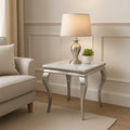 Silver side table with lamp and plant next to a beige armchair in a room with panelled walls.